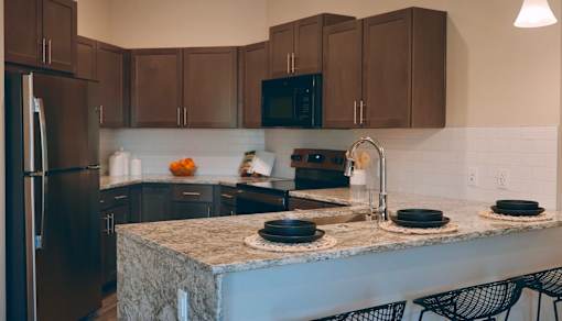A kitchen with a granite countertop and black chairs.