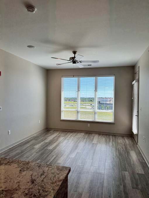 A room with a ceiling fan and a large window with blinds.