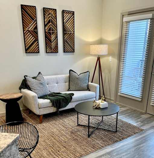 A living room with a grey couch, a black metal chair, and a table with a lamp on it.
