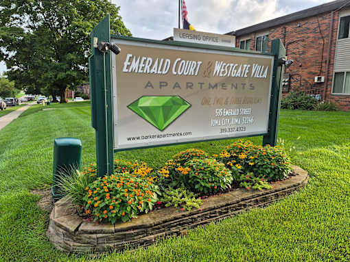 A sign for Emerald Court and Westgate Villa Apartments is surrounded by flowers.