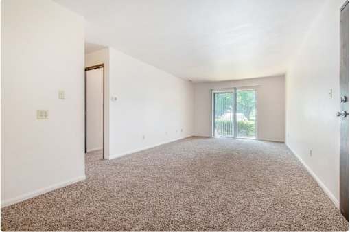 A spacious room with a carpeted floor and a sliding glass door leading to a balcony.
