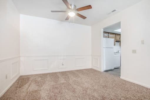 A room with a ceiling fan and a refrigerator in the corner.