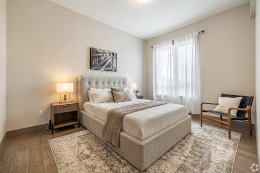 A bedroom with a large bed, a chair, and a painting on the wall.