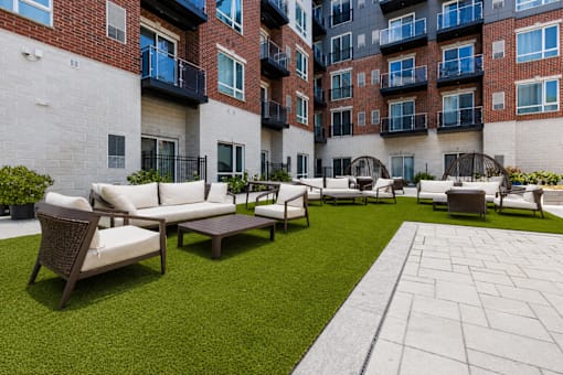 A patio area with a white couch and a green lawn.