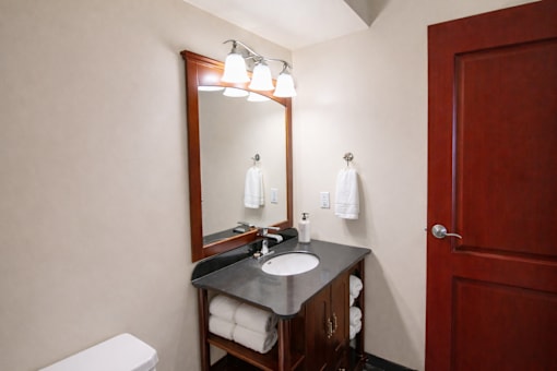 A bathroom with a toilet, sink, mirror, and towel rack.