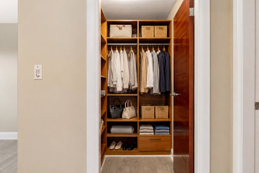 A wooden wardrobe with clothes and baskets on the shelves.