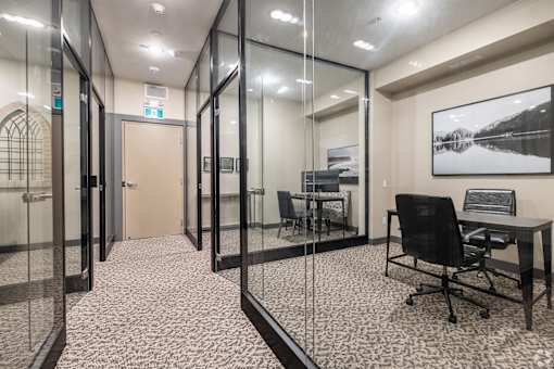 A glass walled office with a black chair and a framed picture on the wall.