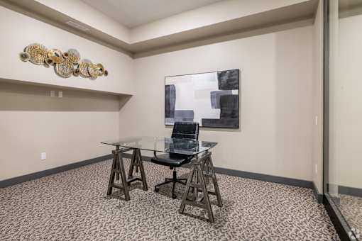 A room with a glass table and chairs and a painting on the wall.