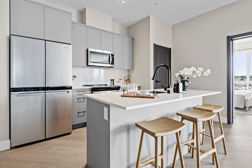 A modern kitchen with a white island and wooden stools at The Woods at 180 Kanata Avenue Apartments, Kanata