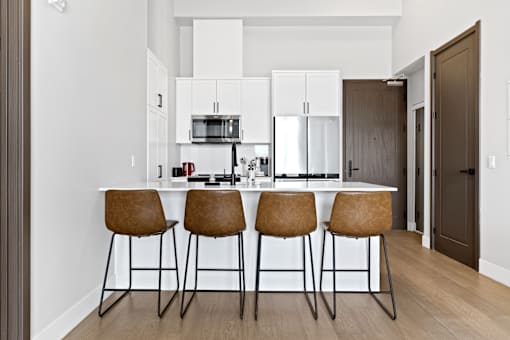 A kitchen with white cabinets and a bar area with brown chairs at The Woods at 180 Kanata Avenue, Kanata, Ontario