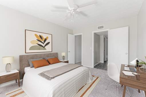 A bedroom with a large bed, a painting on the wall, and a ceiling fan.