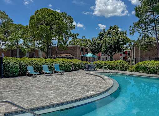 A swimming pool surrounded by a brick patio and lawn chairs.