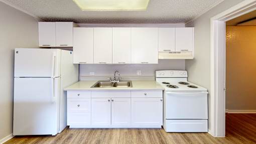 A white kitchen with a refrigerator, stove, and sink.