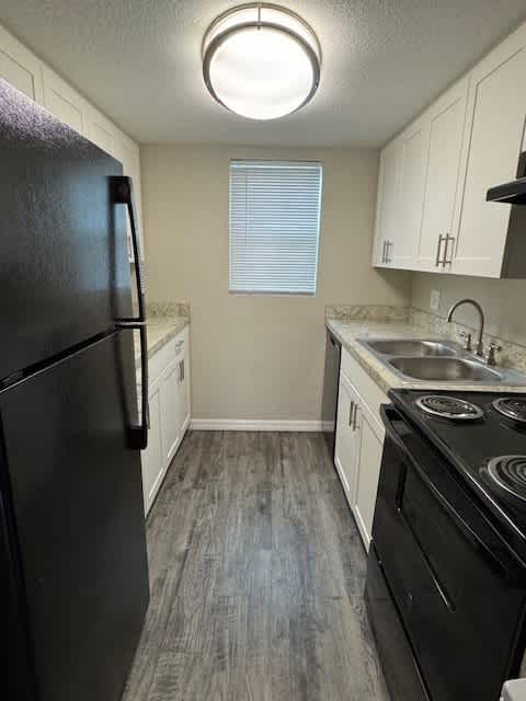 A black refrigerator stands in a kitchen with white cabinets and a black stove.