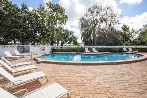 A pool surrounded by trees and chairs.