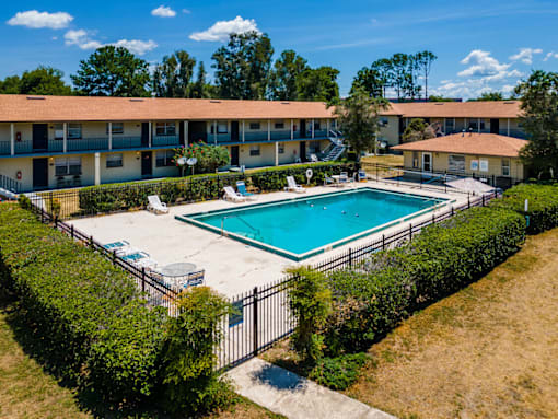A swimming pool surrounded by a fence and bushes in front of a building.