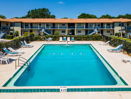 A swimming pool in front of a building with lounge chairs around it.