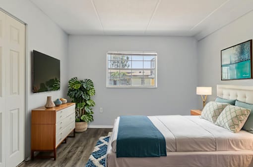 A bedroom with a bed, a dresser, a plant, and a window.
