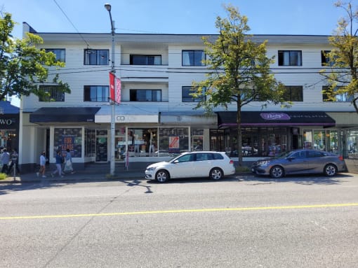 a city street with a large white building in the background and two cars parked in front of