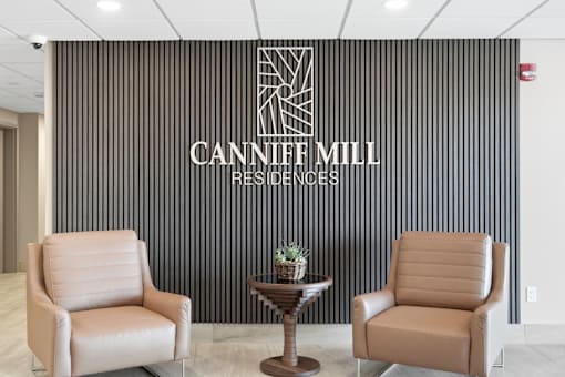 Two leather chairs are placed in front of a black wall with the words "Canniff Mill Residences" written on it.
