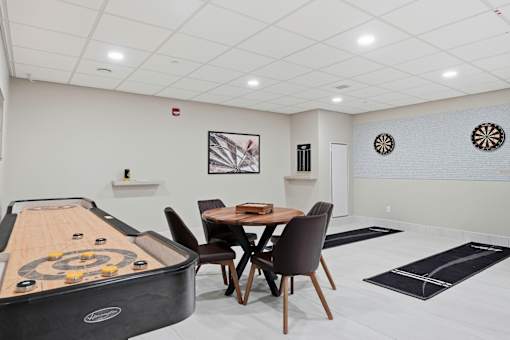 A room with a shuffleboard table and a dining table with chairs.