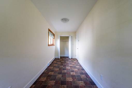 a corridor in a house with white walls and a brown tile floor