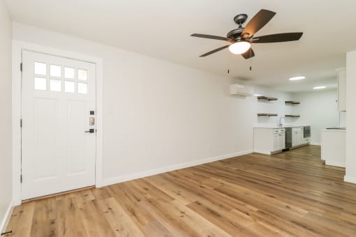 an empty living room with a ceiling fan and a kitchen in the background