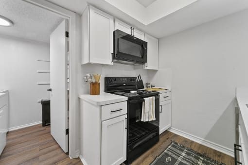 a white kitchen with a black stove and a microwave at Lakeside Apartments, Dallas, TX