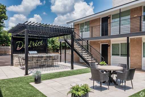 A patio with a table and chairs under a pergola with the word "District" on it.