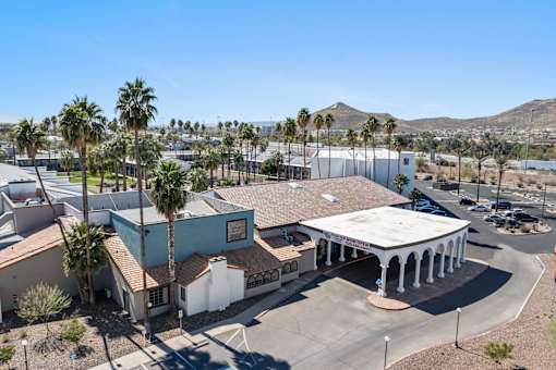 A building with a white roof and a covered patio is surrounded by palm trees at Presidio Palms Apartments, Tucson, AZ