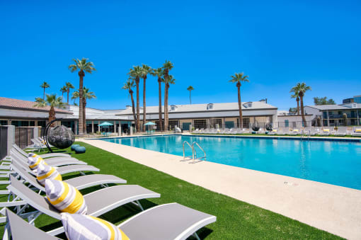 a resort style pool with white chairs and palm trees at Presidio Palms Apartments, Tucson