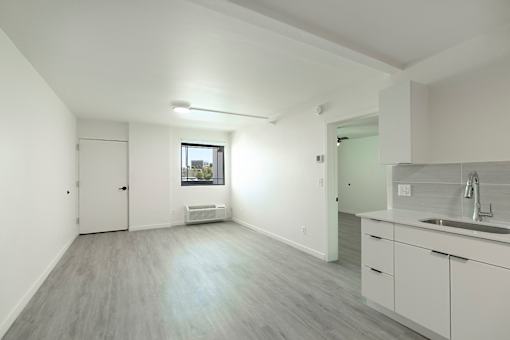 A spacious room with a window, a door, and a kitchen area with a sink and white cabinetsat Presidio Palms Apartments, Tucson, Arizona