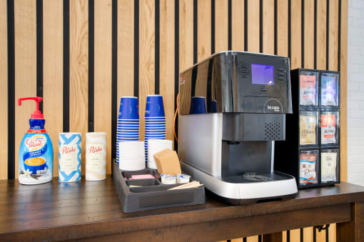 a coffee maker on a table with coffee cups and a napkin dispenser next at Presidio Palms Apartments, Arizona