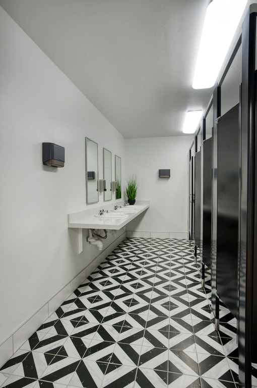 a bathroom with a black and white tiled floor and stalls at Presidio Palms Apartments, Arizona, 85701