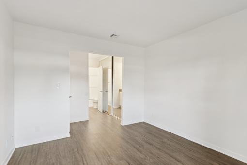 A room with white walls and wood flooring with a doorway leading to another room.