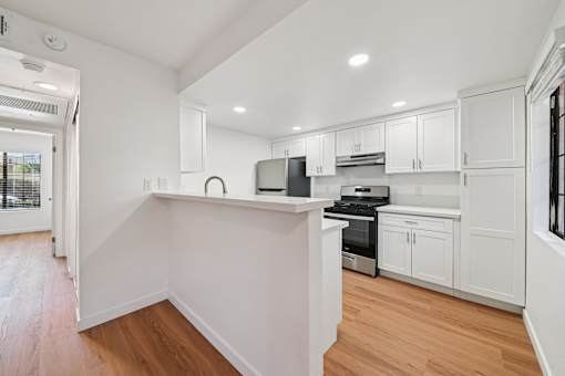A kitchen with white cabinets and wooden floors.