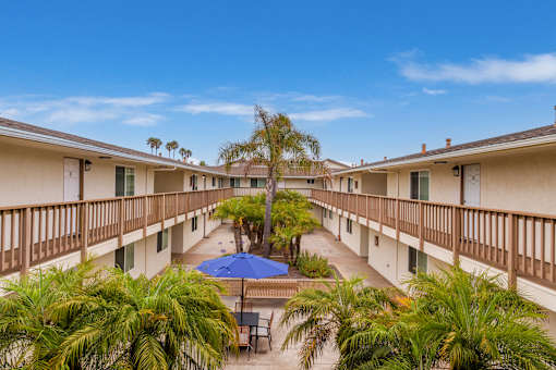A balcony with a blue umbrella and a pool in the middle of the courtyard.