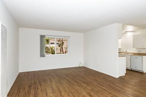 A living room with wooden floors and a window with a view of trees and a building.