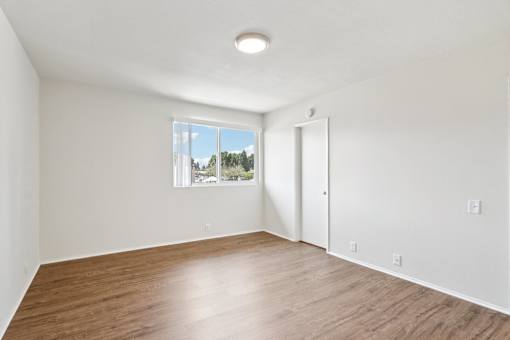 A bedroom with a window and a wooden floor.