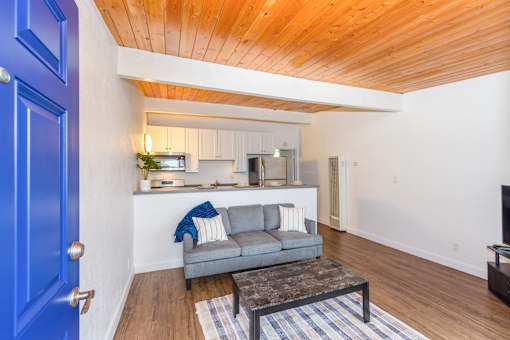 A blue door opens to a living room with a grey couch and a coffee table.