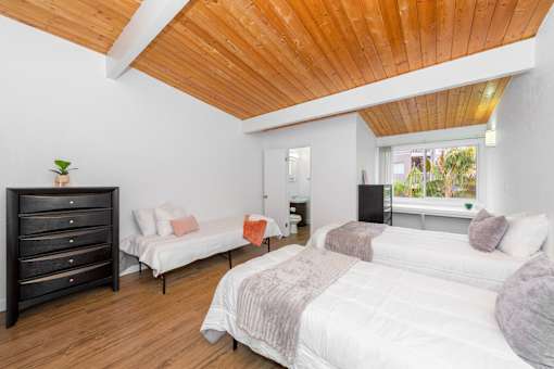 A bedroom with a white bed and a wooden ceiling.
