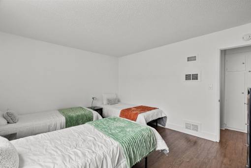 Three beds with green and orange bedspreads in a white room.