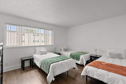 Three beds with white bedspreads and green and brown blankets in a room with wooden floors.