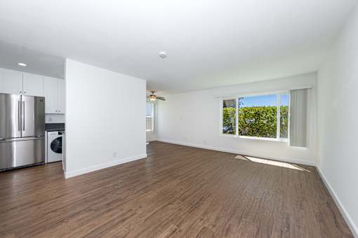 A large living room with wooden floors and a window overlooking a green area.