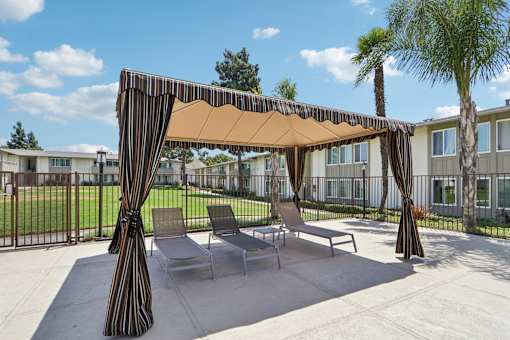 A patio with a striped canopy and chairs.