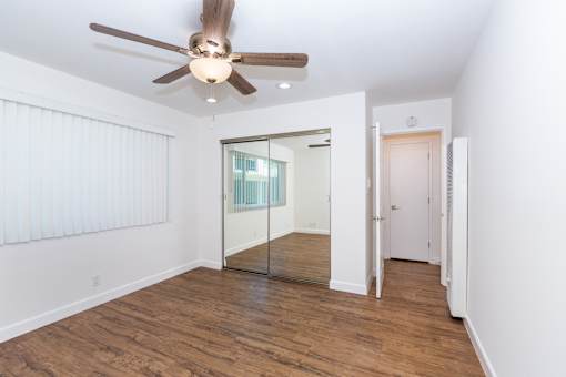 A bedroom with a ceiling fan and wooden flooring.