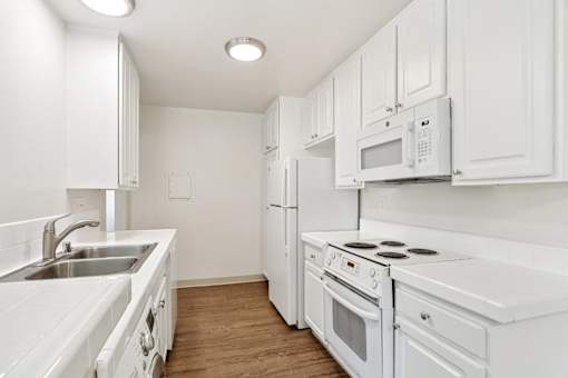 A white kitchen with a sink, stove, and refrigerator.