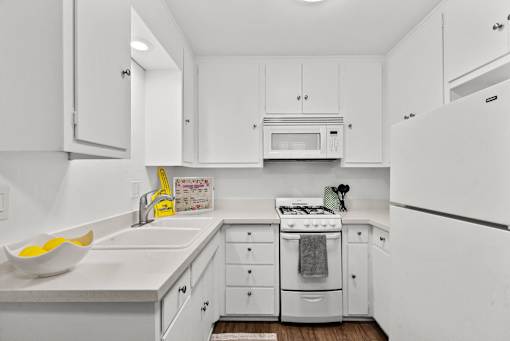 A white kitchen with a sink, stove, and cabinets.
