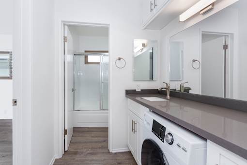 A white bathroom with a sink, mirror, and a washer and dryer.