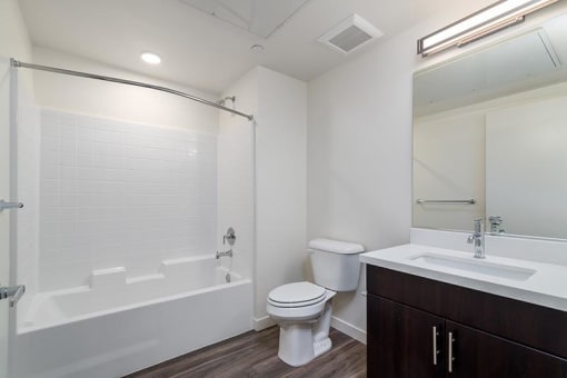 a bathroom with a toilet, sink, mirror, shower/tub combo